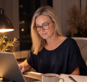 Sharn Rayner studying at night at her desk with a laptop, handwritten notes, a cup of tea and NLP books