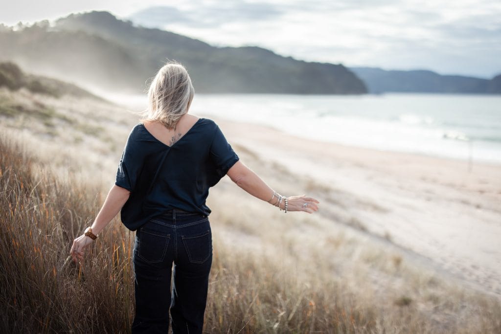 Executive coach Sharn Rayner walking her dog along the Tairua coastline at sunrise, reflecting the daily routine that anchors intentional living.